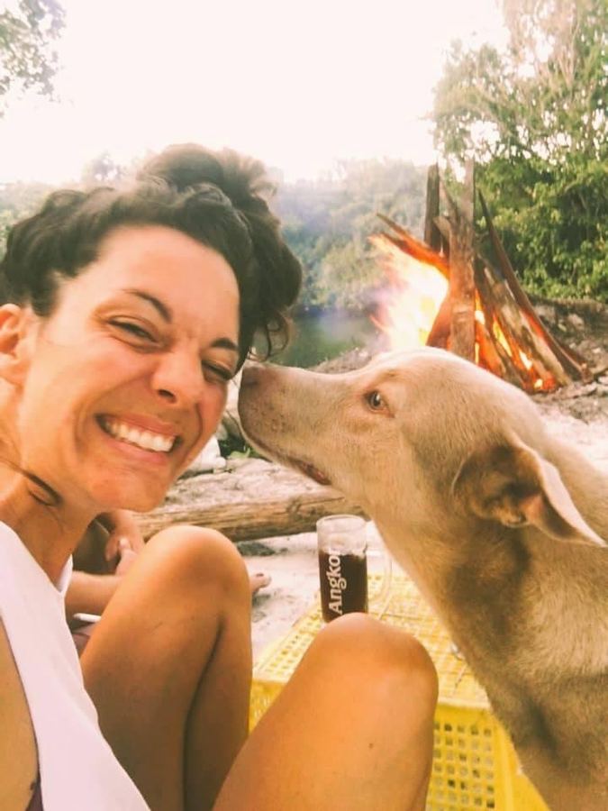 Ein Hund schnuppert an Laura Links Gesicht, dahinter ein Lagerfeuer